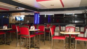 Ein Restaurantinneres mit rot gepolsterten Stühlen und Tischen, einer Theke mit Speisekarte und einem Fernsehbildschirm.