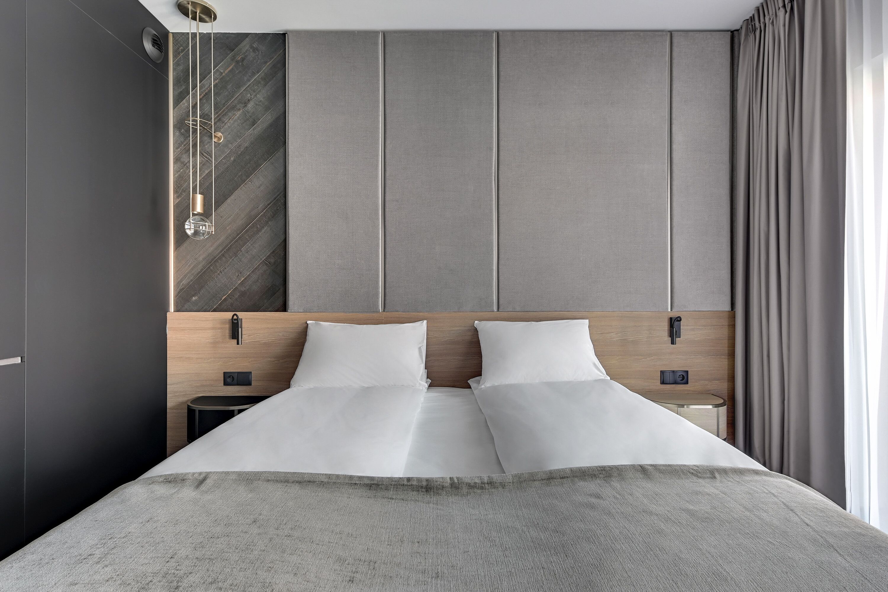 A modern hotel room with a large bed, a wooden headboard, a nightstand, and a small table.