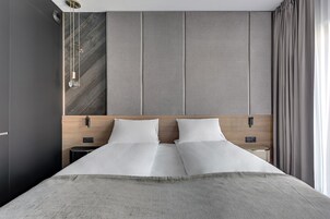 A modern hotel room with a large bed, a wooden headboard, a nightstand, and a small table.