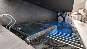 En moderne swimmingpool indendørs med en chevron-mønstret væg, en metalstige og flisegulv.