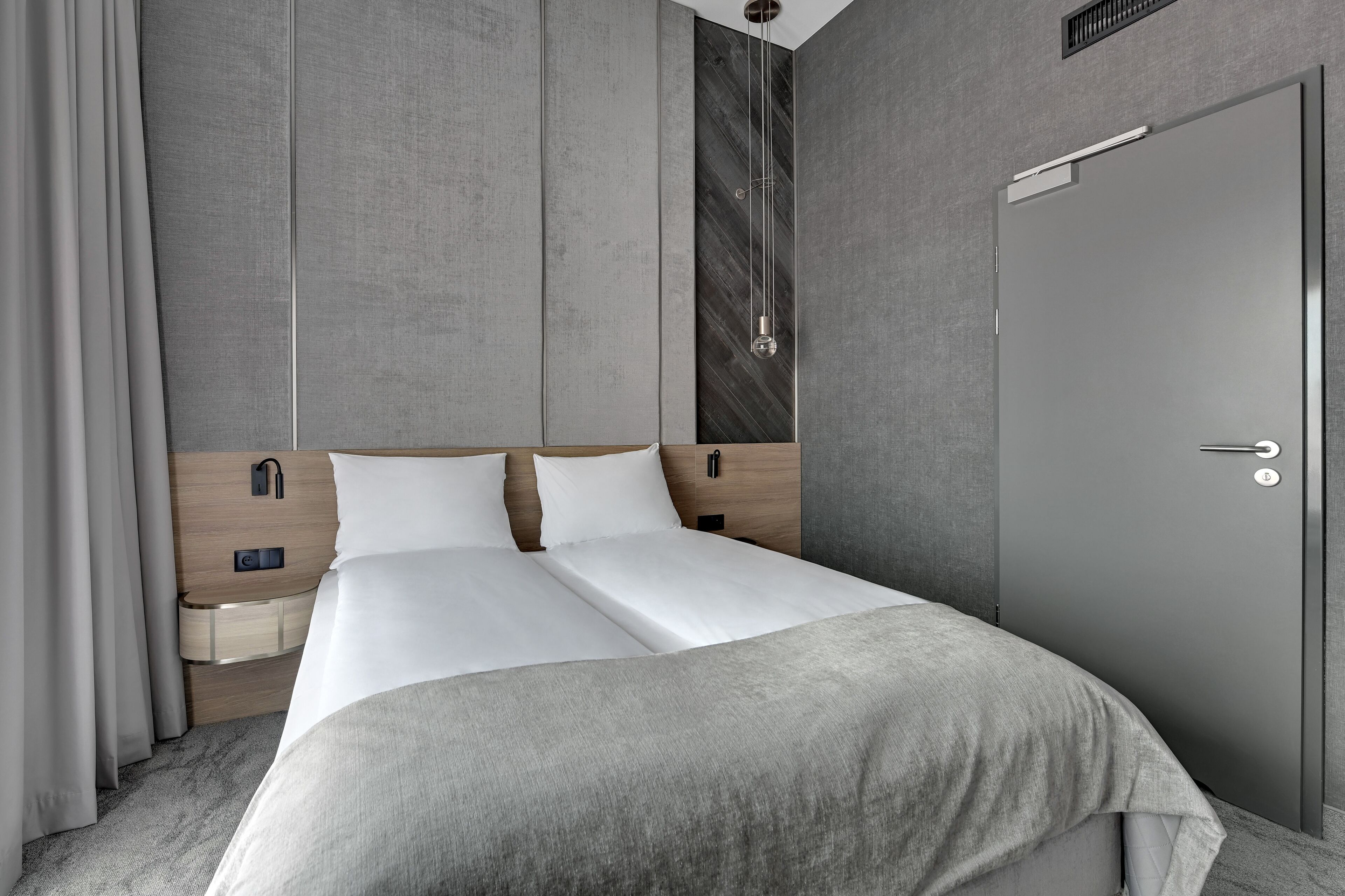 Ein modernes Hotelzimmer mit einem großen Bett, einem Holzkopfstück, Nachttischen und einem Kleiderschrank.