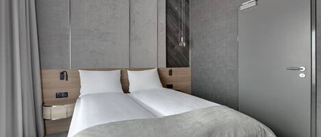 A modern hotel room with a large bed, wooden headboard, bedside tables, and a wardrobe.