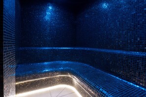 Uma área de estar curva, com azulejos azuis e uma faixa de luz na parte inferior.