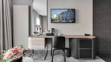 A modern hotel room with a desk, chair, and a large TV displaying a cityscape.