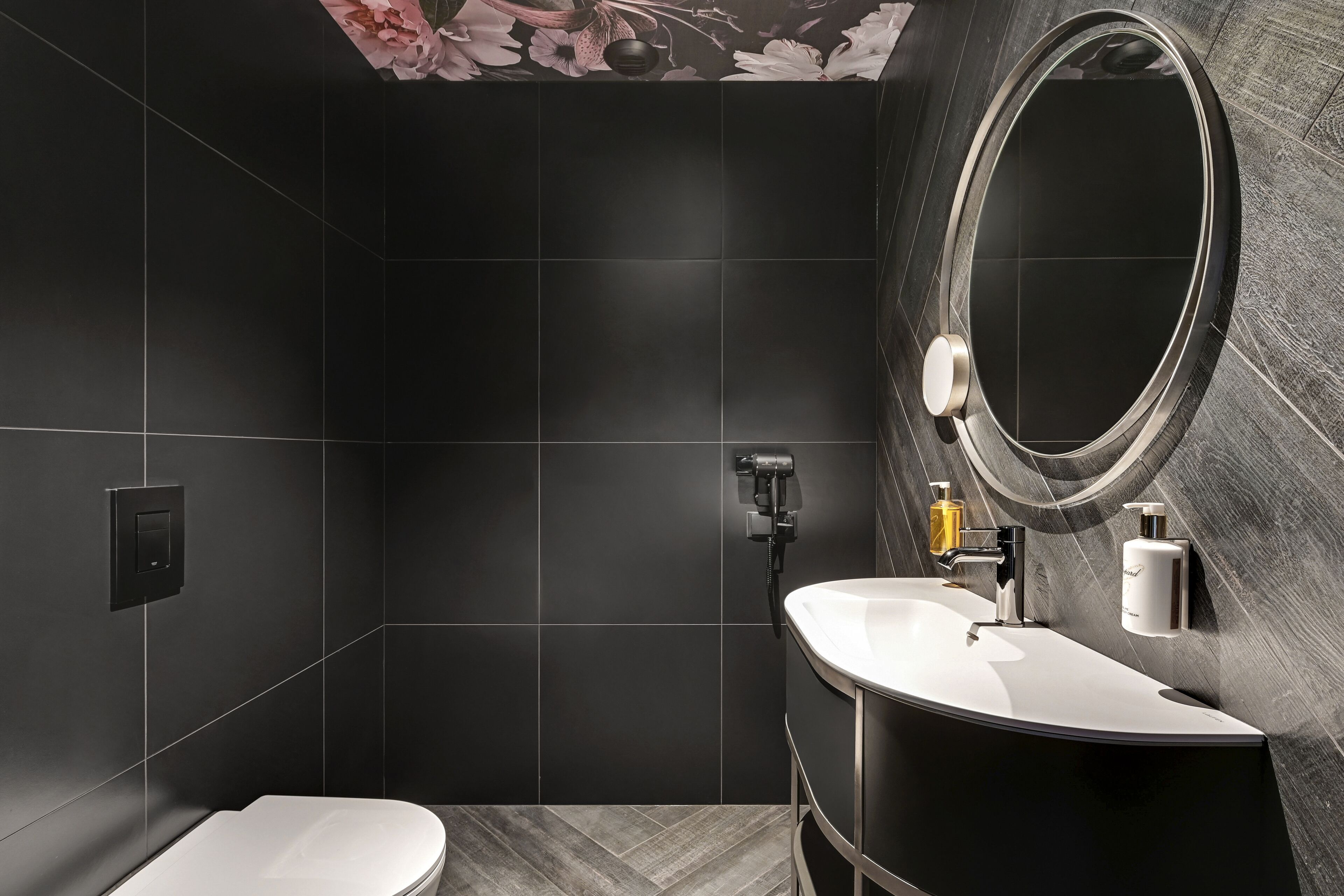 Un baño moderno con un tocador curvo, un espejo redondo y un inodoro.