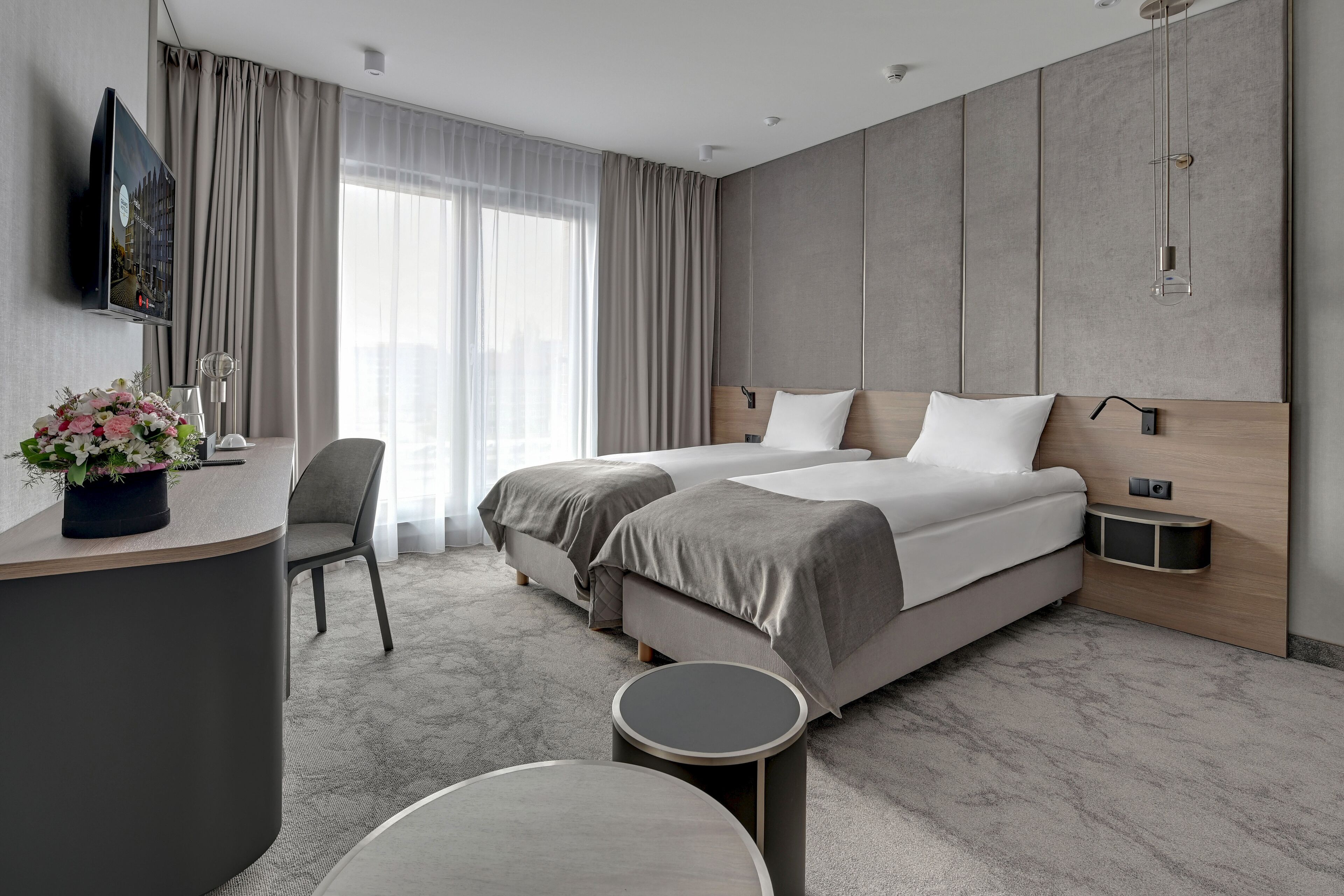 A modern hotel room with two beds, a desk, a chair, and a round table.