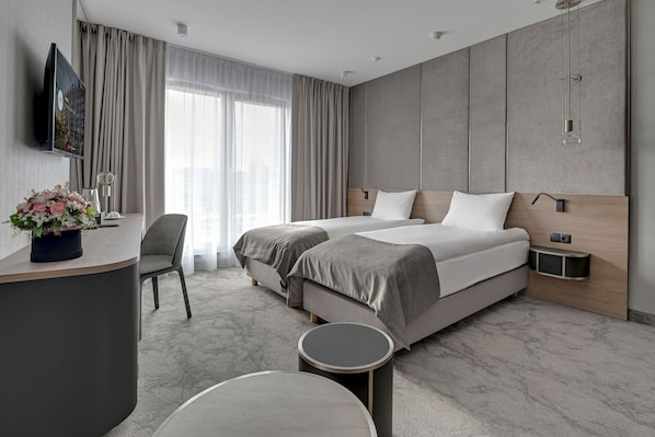A modern hotel room with two beds, a desk, a chair, and a round table. - Grano Hotel**** Gdańsk Old Town (Gdansk)