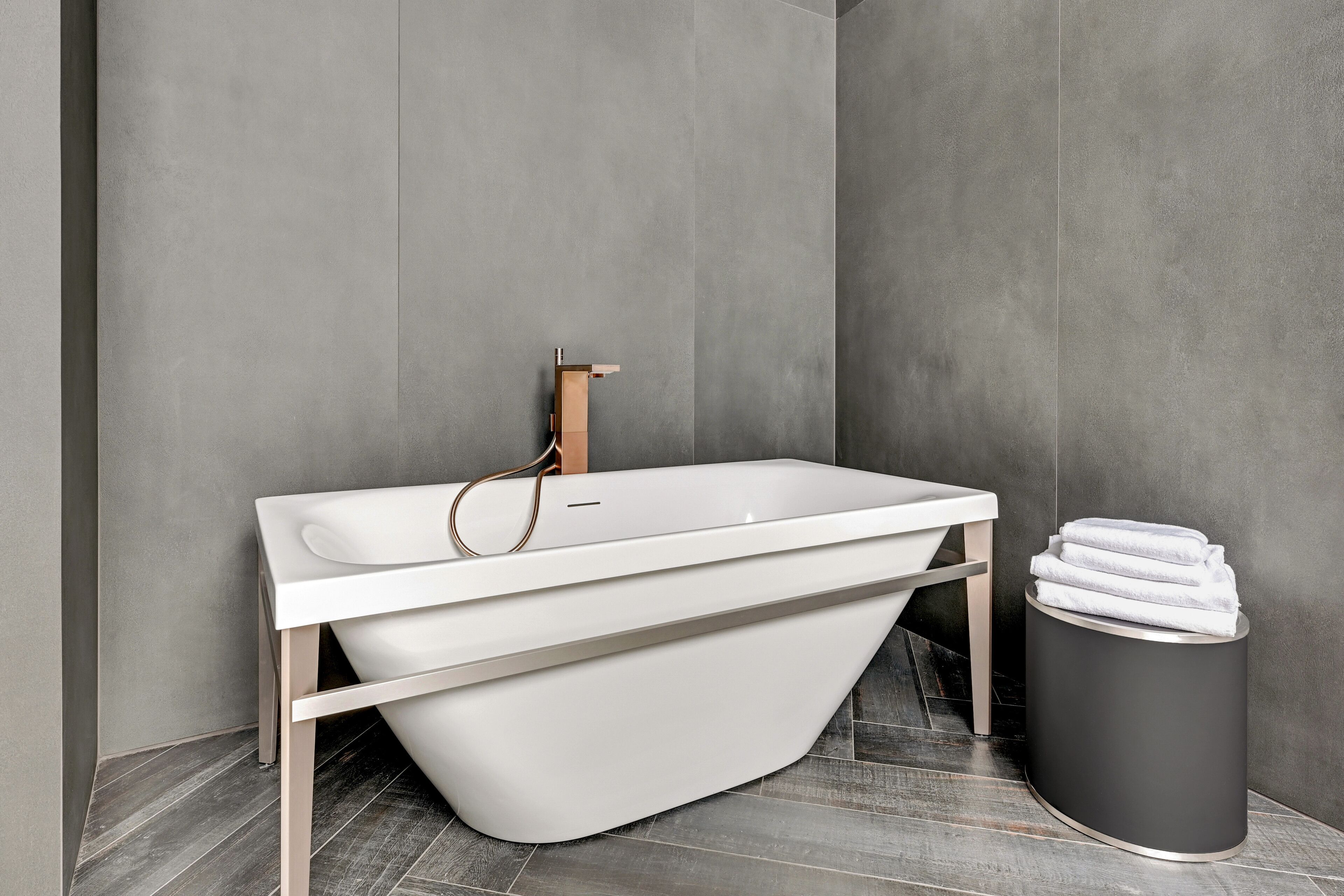 A modern bathroom with a freestanding bathtub, a towel rack, and a trash bin.
