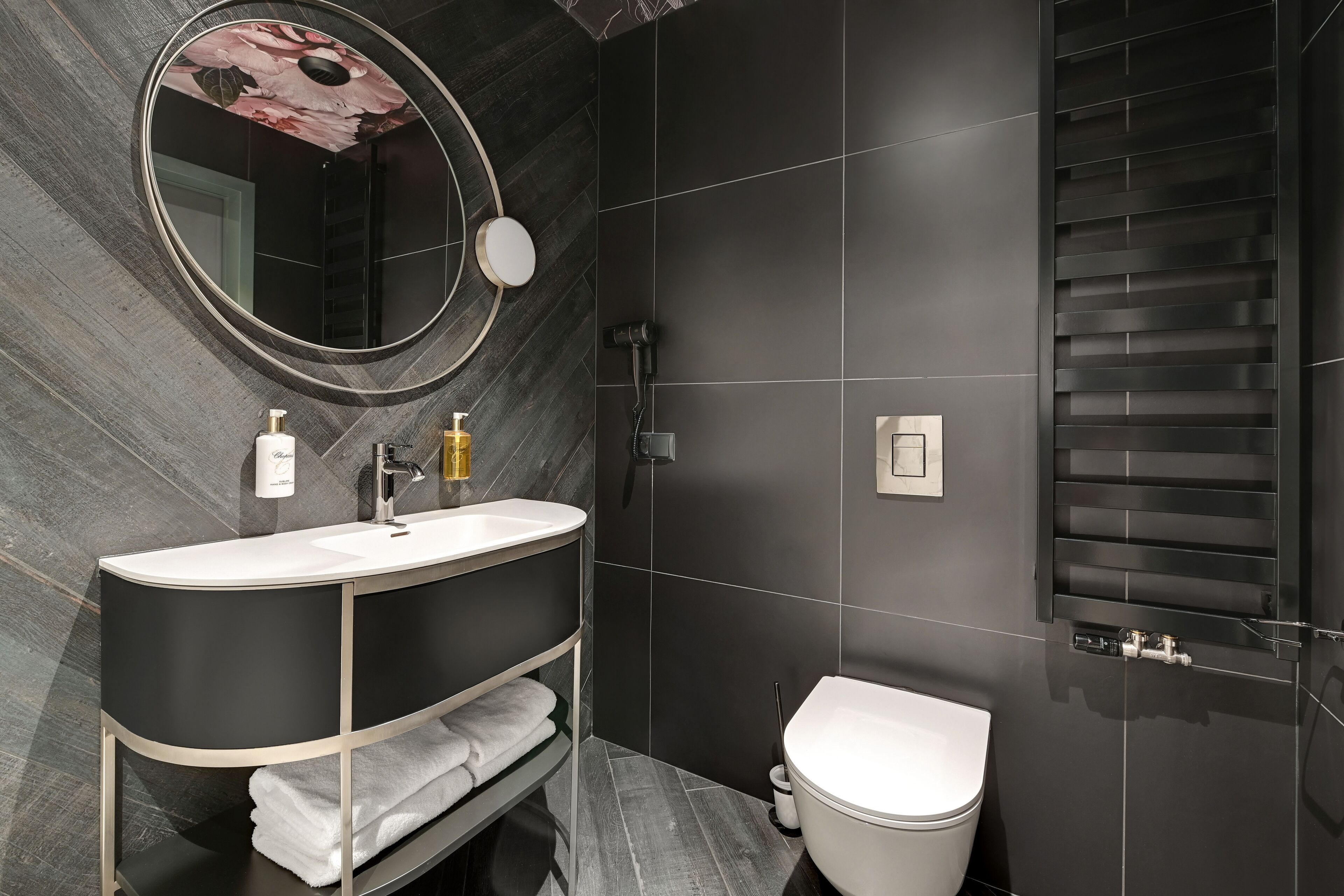 Un baño moderno con un espejo grande, un lavamanos blanco, un inodoro y una zona de ducha.