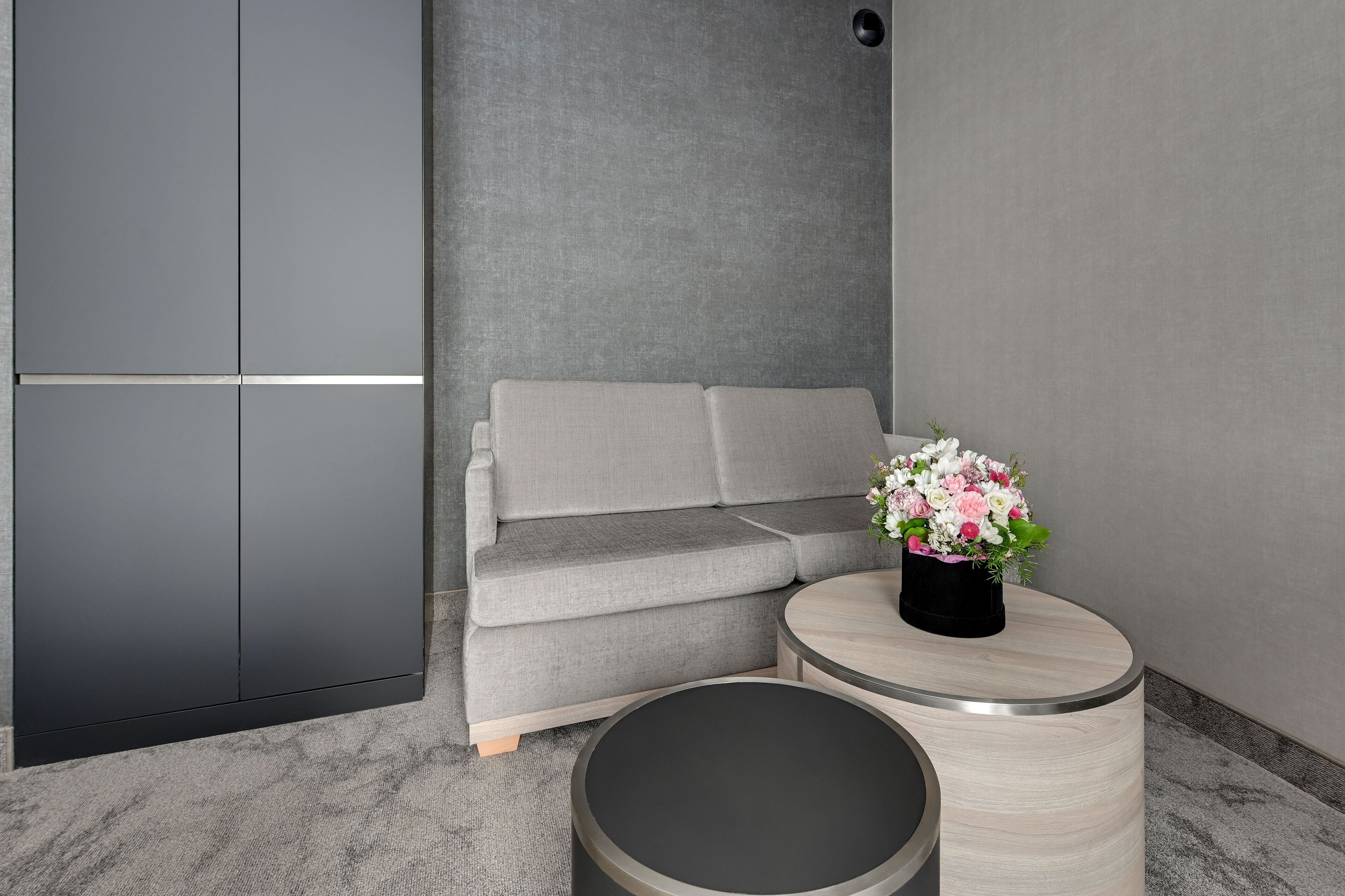 A modern room with a grey sofa, a round table with a vase of flowers, and a grey cabinet.