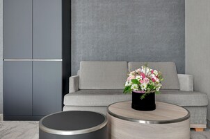 A modern living room with a grey sofa, a round coffee table with a black vase of flowers, and a grey cabinet.