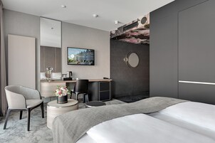 A modern hotel room with a large bed, a desk with a chair, a round mirror, and a television on the wall.