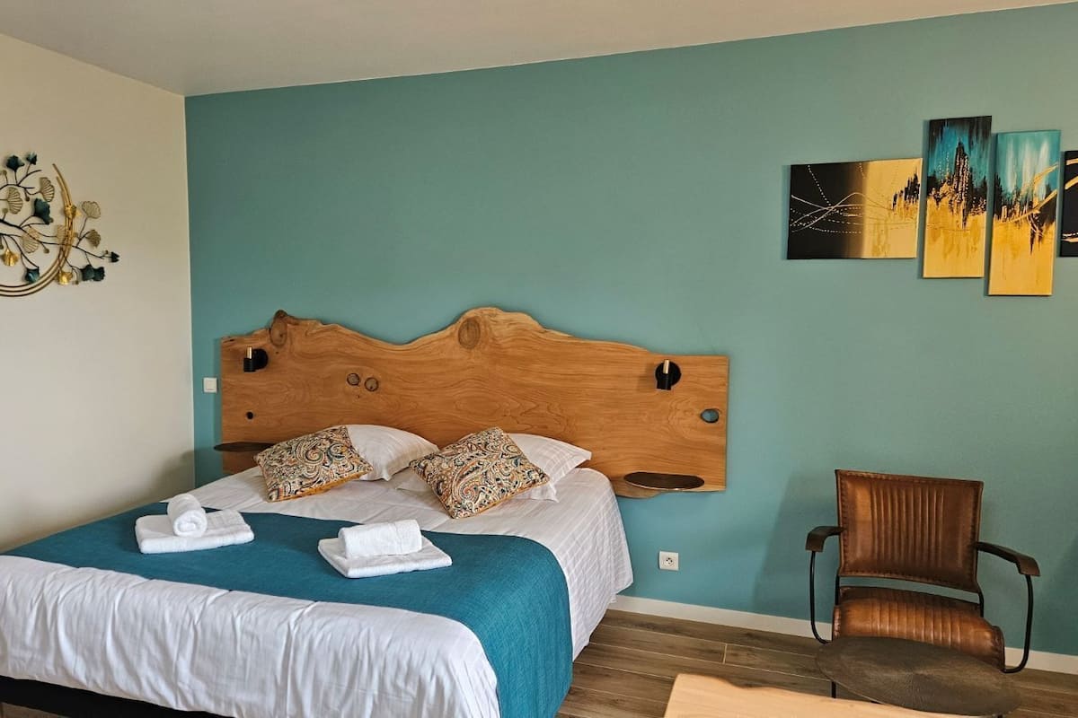 Een slaapkamer met een houten hoofdbord, een bed met witte lakens, meerdere kussens en een stoel.
