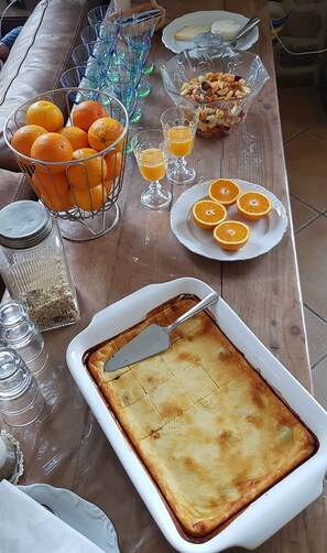 Een eettafel met diverse soorten eten, waaronder een schotel gebakken custard, een fruitschaal en verschillende sinaasappels.