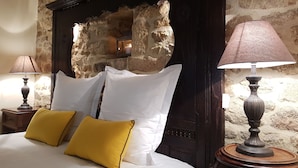 Een bed met witte en gele kussens, een houten hoofdbord tegen een stenen muur, en twee bedlampjes.