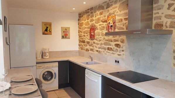 A compact kitchen with a stone wall, a washing machine, a coffee maker, and a dishwasher.