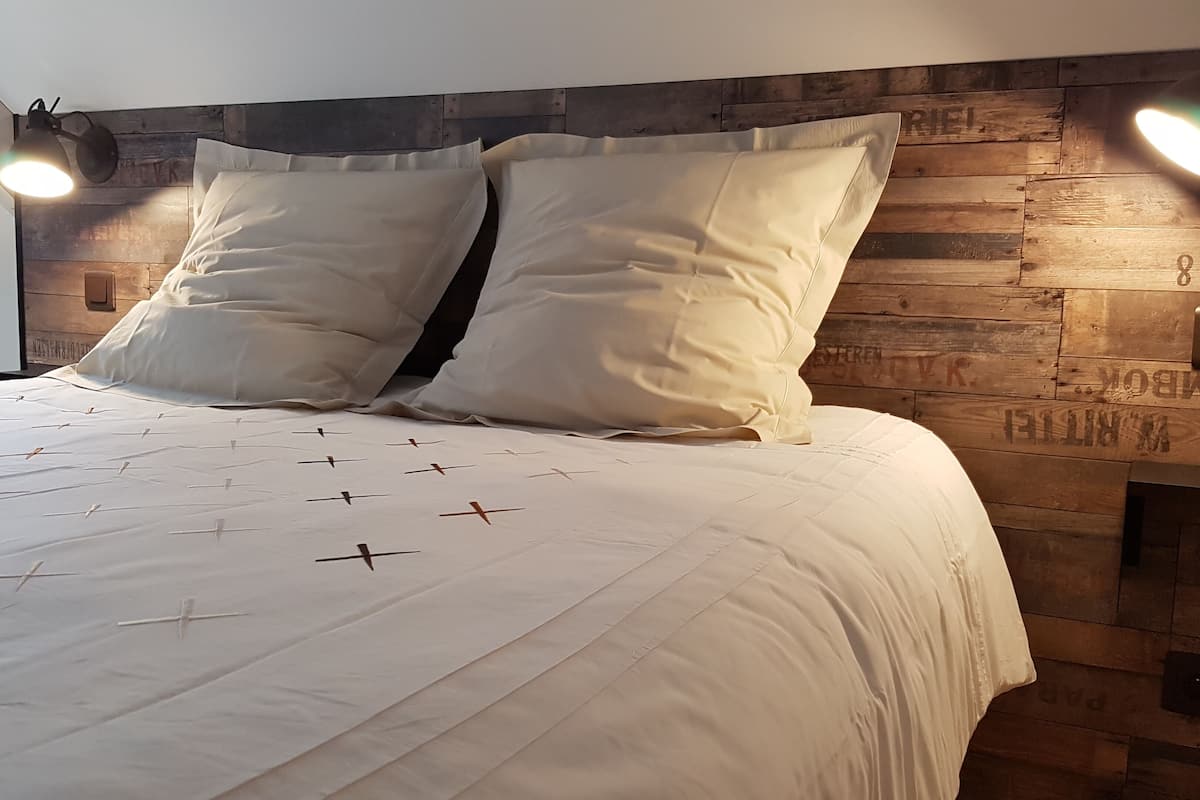 Een bed met wit beddengoed en een houten hoofdeinde met verlichting.