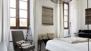 A bedroom with a large bed, a chair, a ladder, and a wall-mounted tapestry. - Le Boutik Hotel (Annecy)