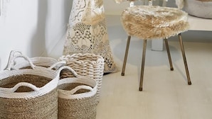 A room with a tall, intricately woven chair, a fluffy stool, and woven baskets on the floor. - Le Boutik Hotel (Annecy)