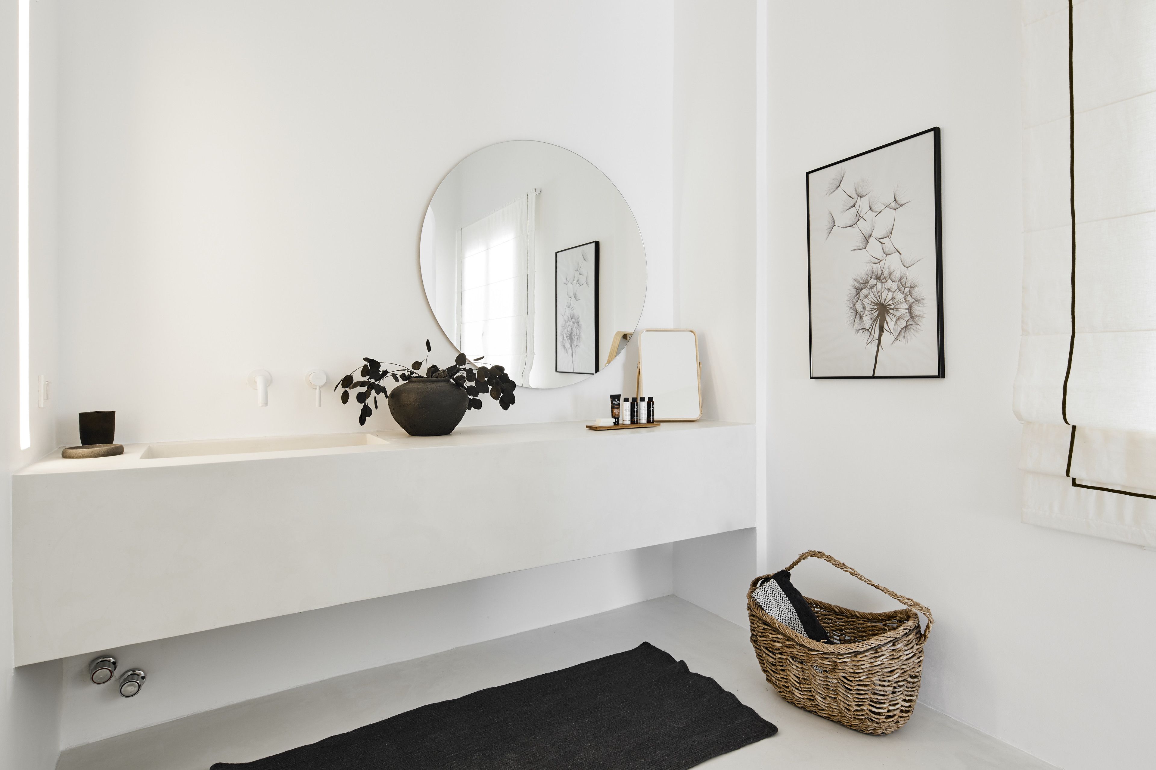 A modern bathroom with a white vanity, a round mirror, a black rug, and a wicker basket.
