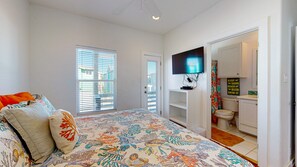 A bedroom with a bed, a television, a bathroom with a toilet and sink, and a window with blinds. - OV37 Shared Pool, Golf Cart Access (Port Aransas)