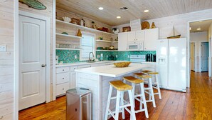 A kitchen with white cabinets, a tiled backsplash, wooden stools, and a central island. - OV37 Shared Pool, Golf Cart Access (Port Aransas)