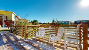 A wooden deck with white chairs, a wooden fence, and a sign warning against casting toward the fountain. - OV37 Shared Pool, Golf Cart Access (Port Aransas)