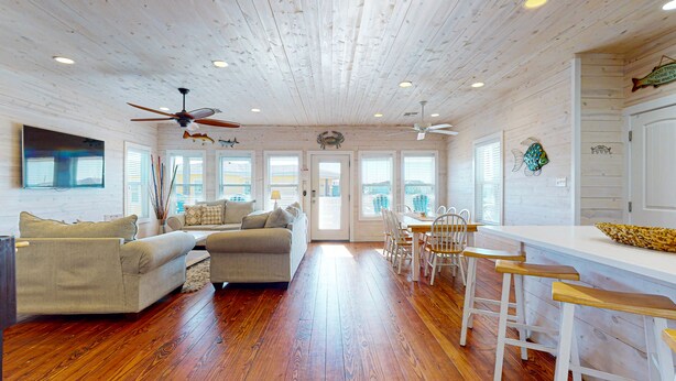 A spacious room with a wooden ceiling, a sofa set, a dining table with chairs, and a bar area. - OV37 Shared Pool, Golf Cart Access (Port Aransas)