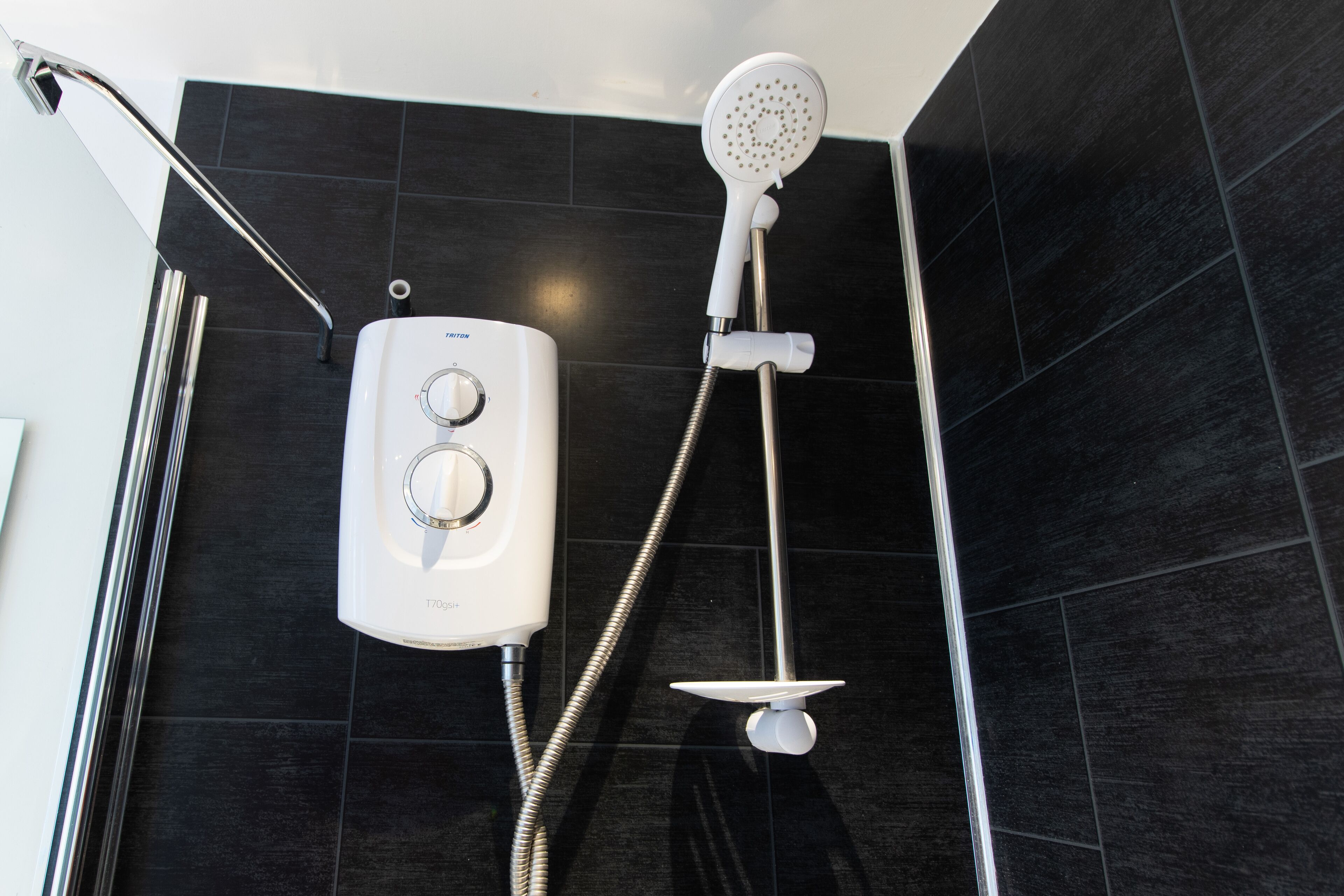 A modern bathroom with a black tiled wall, a handheld showerhead, and a wall-mounted control unit.