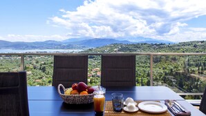 A table with a fruit basket, drinks, and cutlery, overlooking a scenic landscape with mountains and a body of water. - Villa Alba with Private Pool & SeaView (Apolpena)