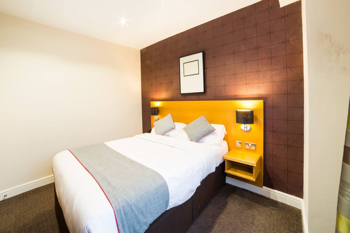 A hotel room with a large bed, two bedside tables, a wall-mounted picture, and a ceiling light.