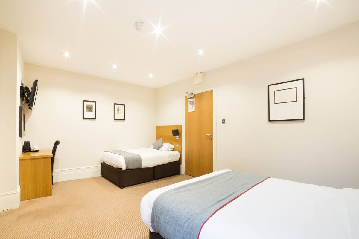 A hotel room with a large bed, a smaller bed, a desk with a chair, and a door.