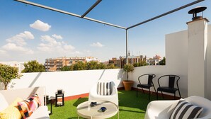 Eine Dachterrasse mit einer weißen Couch, zwei Stühlen, einem kleinen runden Tisch und einem Blumentopf.