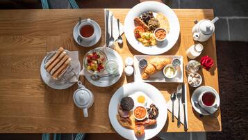 A wooden table with breakfast items including toast, eggs, sausages, and a variety of spreads.