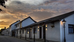 A row of white buildings with a covered walkway and hanging flower baskets. - The Skye Inn (Portree)