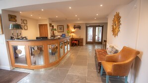 A spacious living area with a curved wooden coffee table, a brown leather sofa, and a dining table with chairs. - The Skye Inn (Portree)