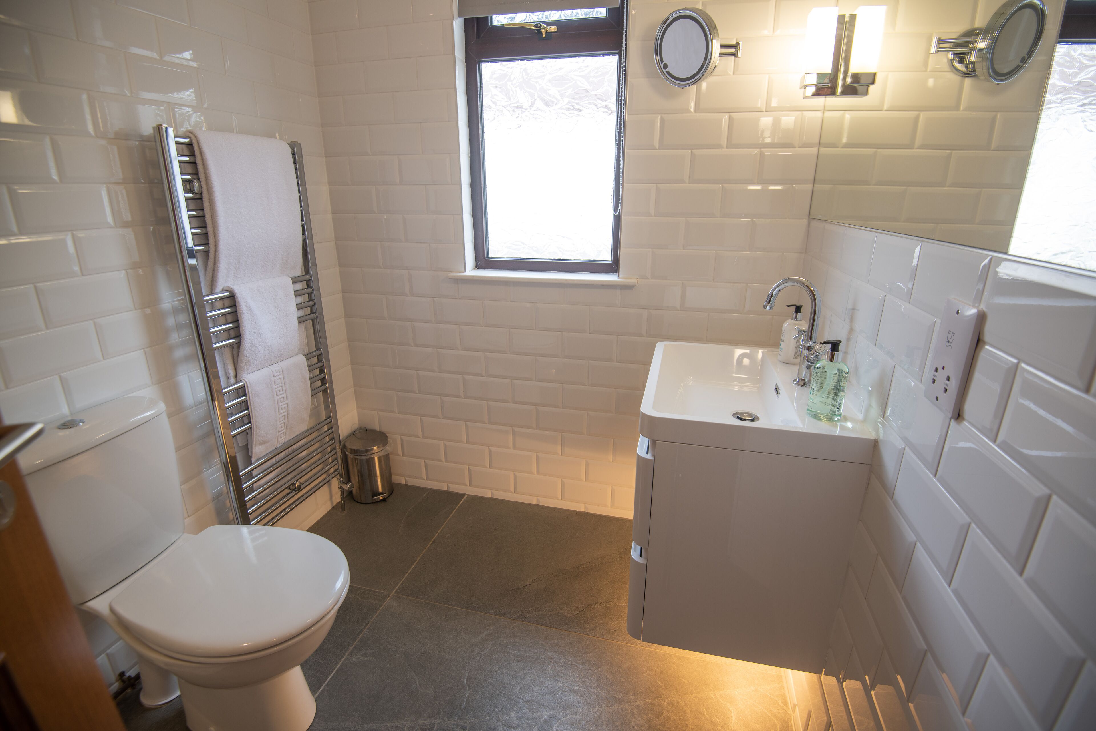 A bathroom with a toilet, a sink, a mirror, and a window.