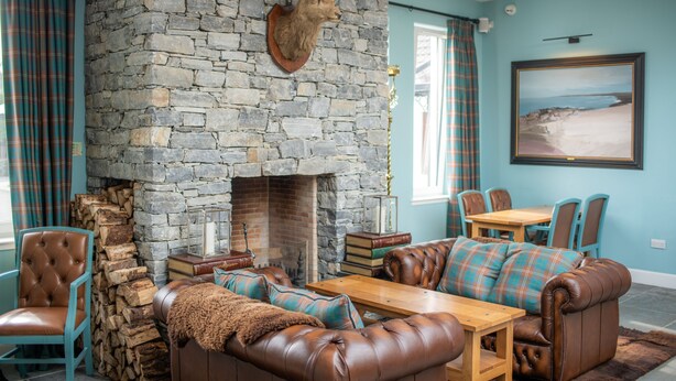 A cozy living room with a stone fireplace, leather furniture, and plaid curtains. - The Skye Inn (Portree)
