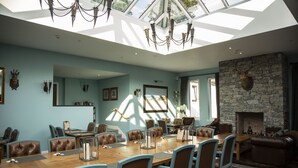 A spacious room with a large wooden table, leather chairs, a stone fireplace, and a chandelier. - The Skye Inn (Portree)