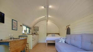 A compact, single-room accommodation with a kitchenette, a dining area, and a bed. - Orchard Farm Luxury Glamping (Glastonbury)