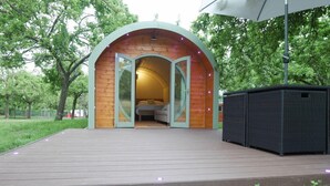A circular wooden structure with a glass door entrance, a bed inside, and a small outdoor seating area. - Orchard Farm Luxury Glamping (Glastonbury)