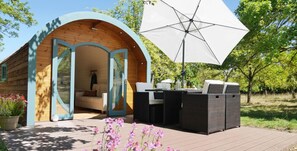 Een houten blokhut met een open boogvormige doorgang naar een gemeubileerd terras, inclusief een tafel en stoelen.