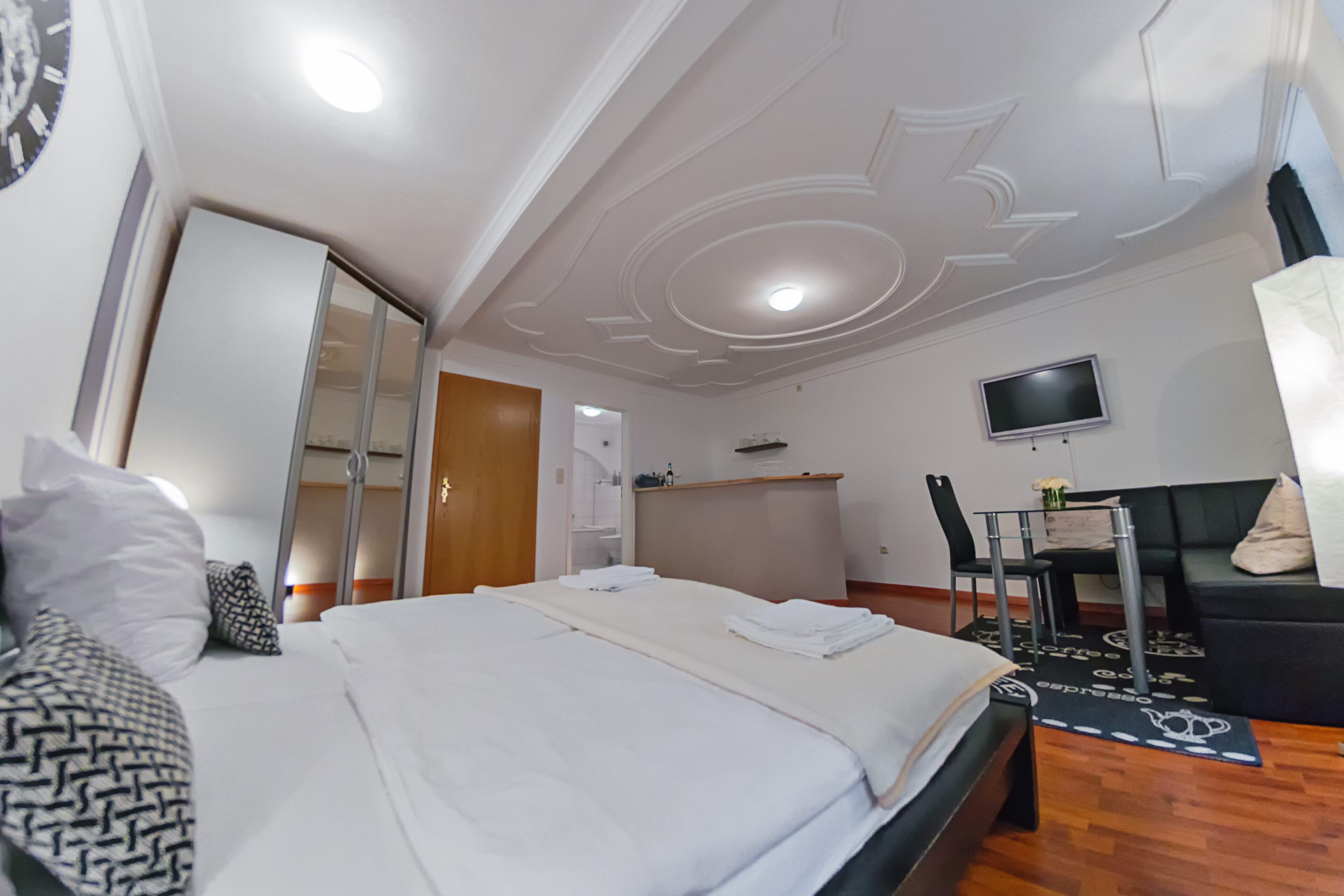 A hotel room with a neatly made bed, a television mounted on the wall, and a seating area with a sofa and chairs.