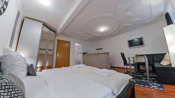 A hotel room with a neatly made bed, a television mounted on the wall, and a seating area with a sofa and chairs.