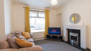A living room with a sofa, television, fireplace, and a window with curtains. - Old Shop (Newport)