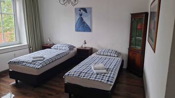 A room with two beds, a painting on the wall, a window with curtains, and a wooden cabinet.