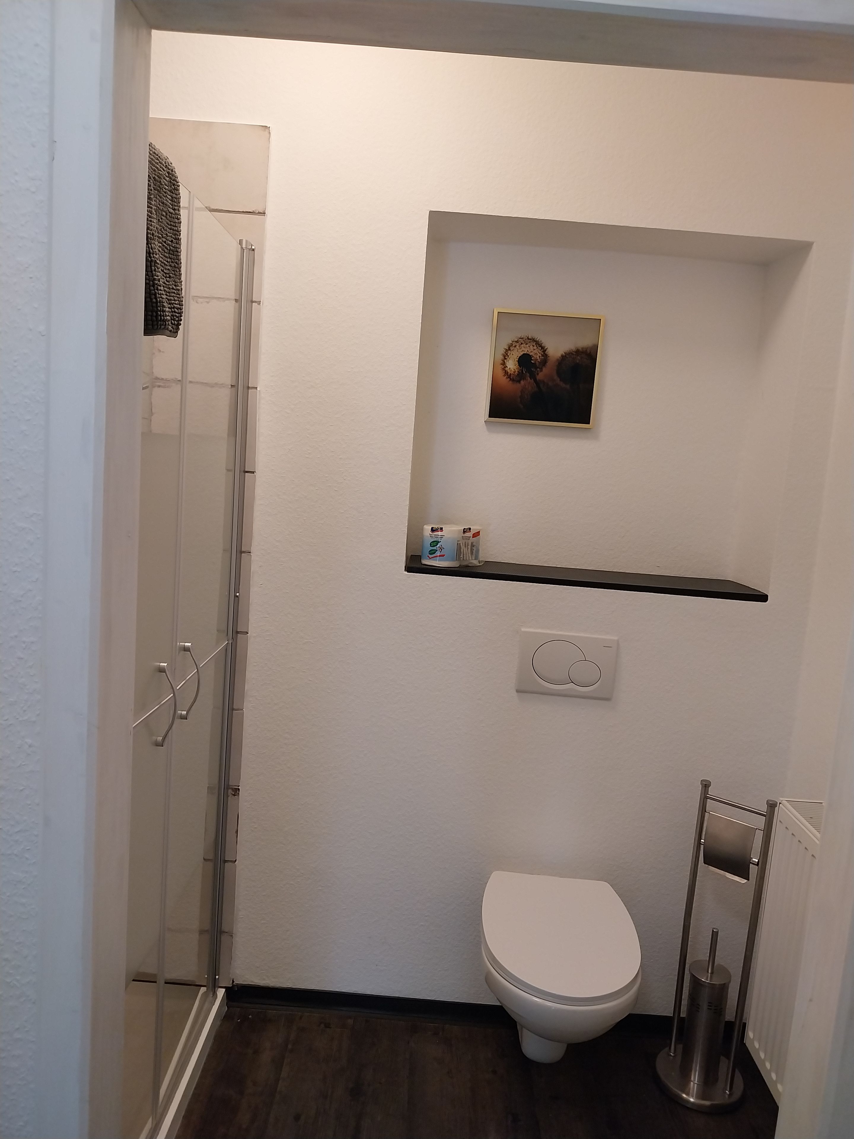 Ein Badezimmer mit Dusche, Toilette und Ablage für Toilettenartikel.