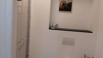 Un baño con ducha, inodoro y estante con artículos de aseo.