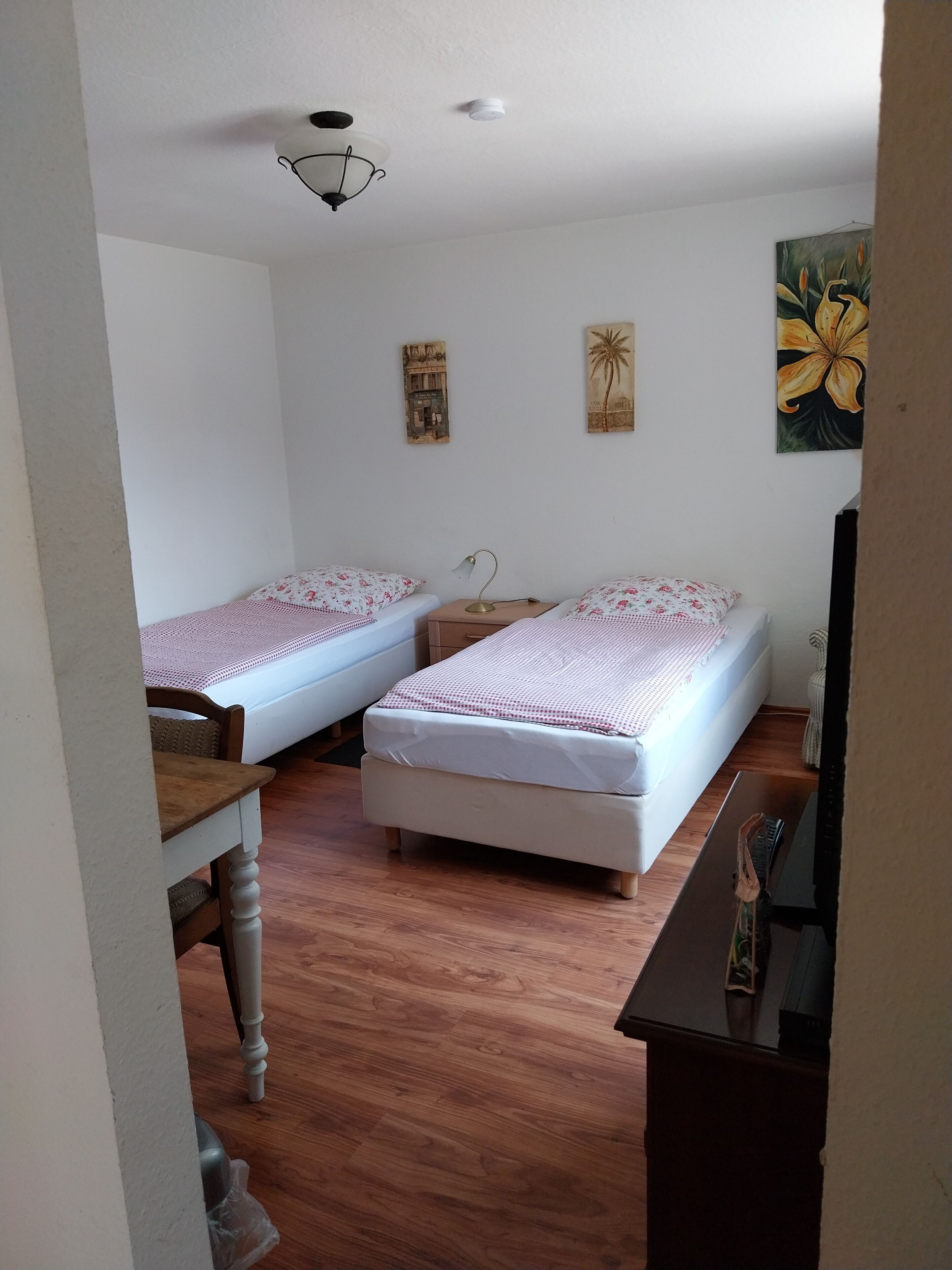 Un dormitorio con dos camas individuales, un escritorio de madera, una silla, una lámpara y un cuadro en la pared.