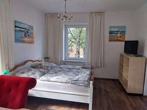 A bedroom with a bed, a television on a stand, a window with curtains, and two paintings on the walls. - Zimmervermietung Hohenlockstedt (Hohenlockstedt)